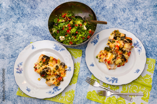 Baked Vegetable Casserole of Broccoli made with Chicken, Potato, Sweet Bell Red Pepper, Cheese and Tomatoes on Plates and Raw Salad of Fresh Iceberg Lettuce with Tomatoes, Olives, White Salad Cheese, 
