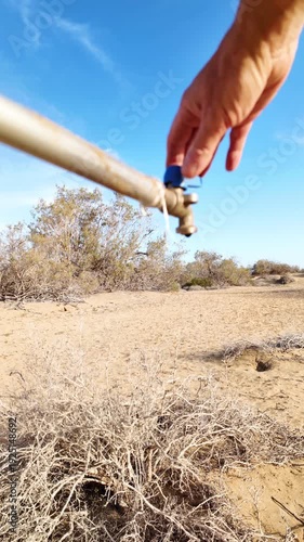 Male hand turning off a tap to prevent precious drops of water from falling into the arid desert soil, symbolizing the devastating impact of global warming, climate change, water scarcity and drought