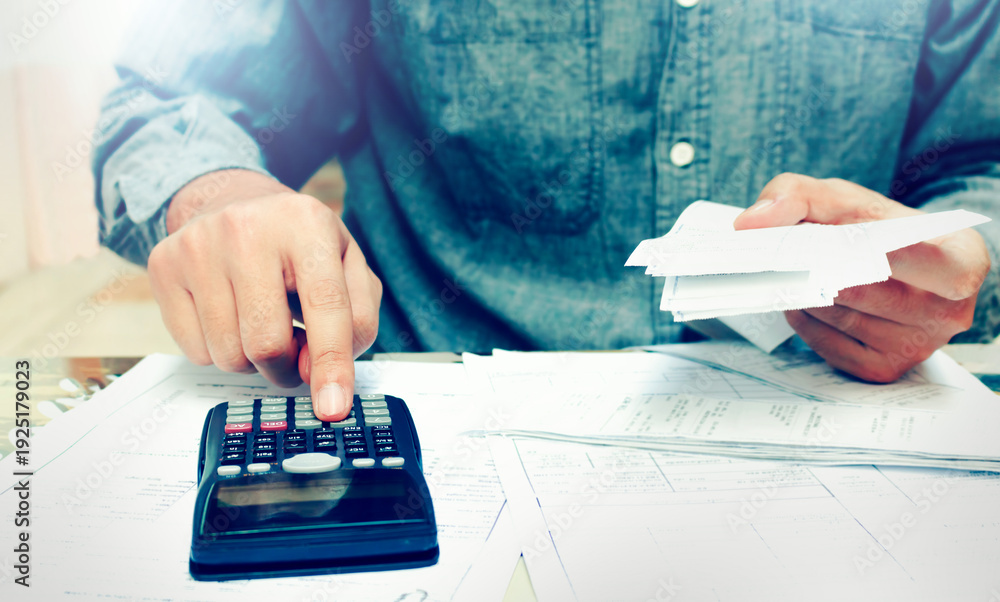 Fototapeta premium Young asian man using calculator and calculating bills to budgeting and tax calculation monthly expenses. budget management and accounting on table at home.