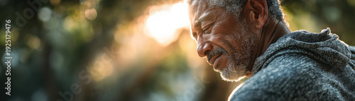 Senior man portrait outdoors sunlight hoodie thoughtful beard, gray hair and wrinkled face in warm golden hour, quiet reflective mood, soft bokeh background in park
