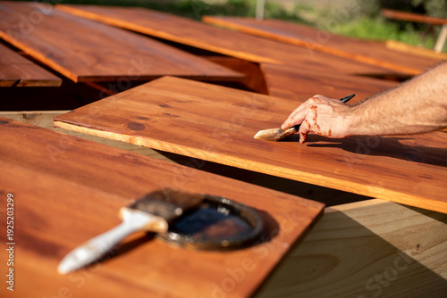 Photography Hand applying wood stain outdoors on timber boards
