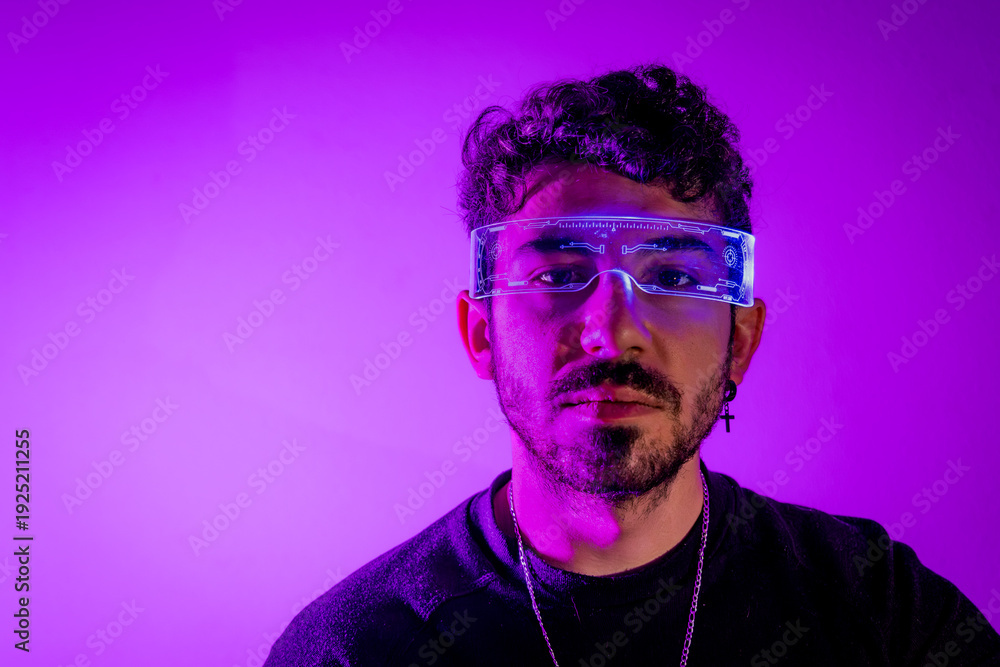 Obraz premium Man wearing augmented reality glasses, looking at viewer in purple neon light
