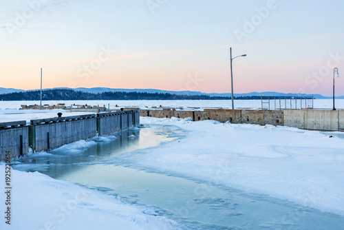 Islands in partly frozen St. Lawrence river seen at sunset, with old and more recent village piers in the foreground, Kamouraska, Québec, Canada