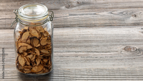 Dried Asian pear slices in a glass jar on a rustic wooden boards background. Dried healthy homemade fruit snacks. Free space for additional content.