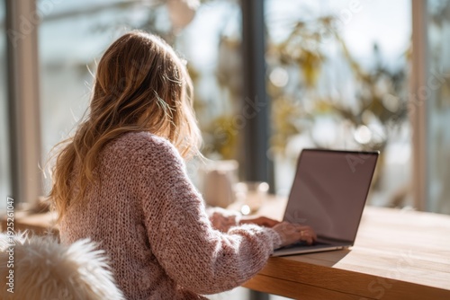 Woman working on laptop in sunlit home workspace