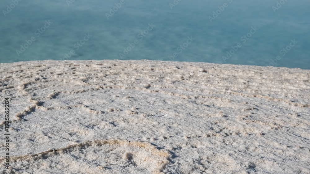 Obraz premium Close-up of white sea salt crystals on the Dead Sea shore in Israel with turquoise water background.