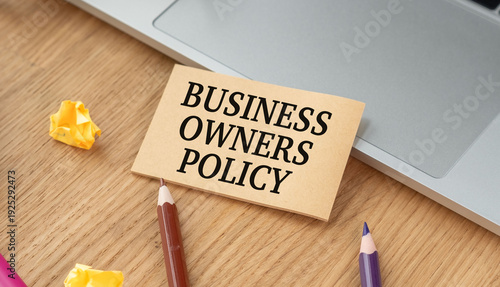Fotografi Business Owners Policy (BOP) text on a craft card on a wooden desk with a laptop and pencils