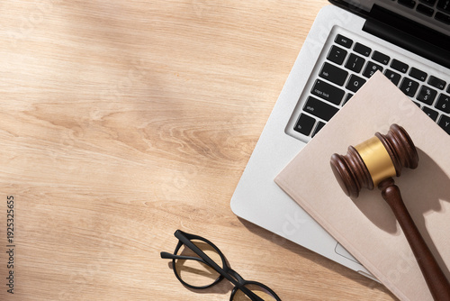 Fotografie A wooden gavel with gold band sits on a light wooden desk beside a laptop, beige notebook and eyeglasses, evoking a modern legal workspace under soft lighting