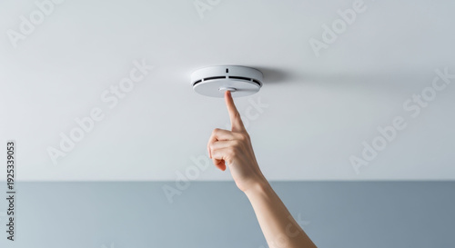 Hand pressing a smoke detector button on the ceiling, performing a routine safety check to ensure fire protection in a modern home.