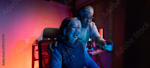 Senior couple, excited senior eldery Asian woman and man with headphones streamer playing video game using desktop computer at gaming room at home. colorful neon background