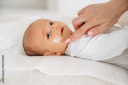 Slika na platnu Infant with light brown hair lying on a soft surface while a hand applies cream