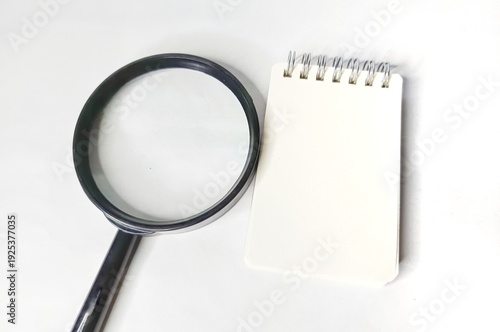 Magnifying glass and blank notebook on white background