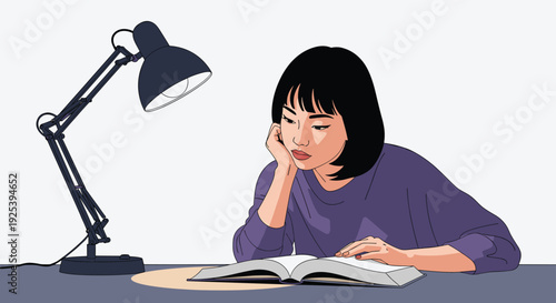 Young woman sitting at her desk and reading a thick book under the light of a black desk lamp in a quiet room at night.