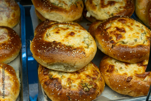 Homemade baked buns with savory cheese and meat filling. Delicious variety of snack vatrushka buns with cottage cheese herbs and ham pieces on a metal tray.
