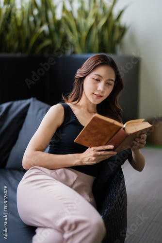 Woman sitting comfortably on a sofa, engrossed in reading a book, finding a moment of peace and relaxation in her lifestyle, surrounded by lush indoor greenery in a quiet setting
