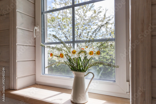 Spring daffodils in white ceramic jug on wooden windowsill with soft natural light interior