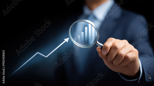 Businessman in suit holding magnifying glass analyzing stock market growth chart with success feeling business investment profit concept