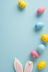 Happy Easter vertical greeting featuring pastel decorated eggs and bunny ears arranged on a soft blue background for seasonal celebration and spring decor