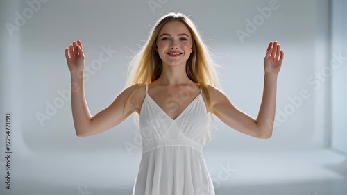 Young Woman in White Dress Smiling and Raising Arms in Studio With Soft Lighting