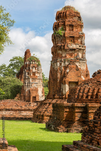 Two ancient, weathered red-brick prangs (temple towers) in the Ayutthaya historical park, Thailand. The towers are heavily textured with centuries of erosion and feature several decorative tiers.
