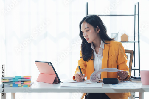 Focused Professional: A poised individual meticulously reviews documents while utilizing a digital tablet, reflecting concentration and dedication in a modern workspace.