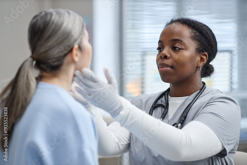 Foto Black young adult woman doctor examining face of Caucasian middle aged woman pat