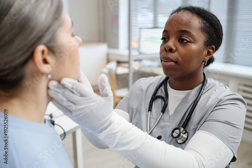 Fotografija Young adult Black female doctor examining face of Caucasian middle aged woman pa