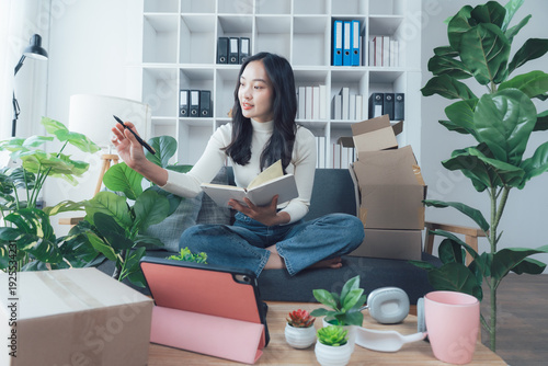 A Moment of Serenity: In a sunlit home office, a young woman finds balance amidst the lush greenery. Dressed casually, she appears focused, perhaps sketching or jotting ideas in her notebook.