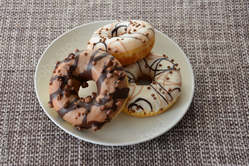 Three Delicious chocolate and cream Glazed Donuts with Sprinkles on a Plate