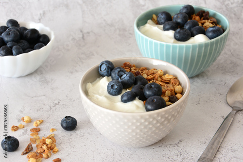 Bowls with Fresh Blueberries, yogurt and Granola on marble background close up