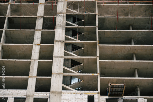Concrete building under construction with exposed stairwell and scaffolding