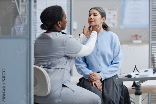 Bild auf Leinwand Black woman doctor examining neck of middle aged Caucasian woman during medical