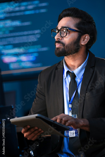 Принти на полотні An Indian male software engineer or data scientist holds a tablet in a command center