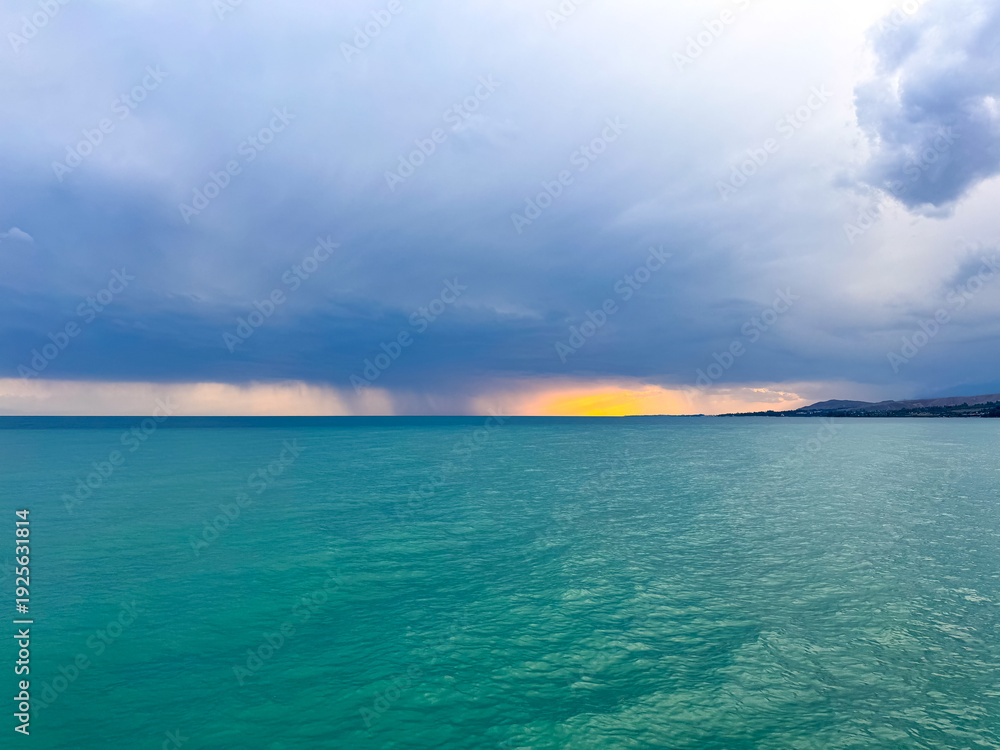 Fototapeta premium Sunset at Issyk Kul Lake in Kyrgyzstan. Bright sun breaking through clouds reflecting in clear turquoise water.
