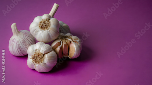 A vibrant purple background showcases a pile of fresh garlic bulbs