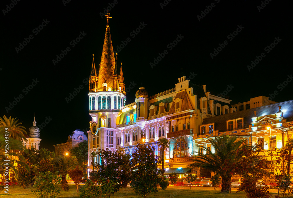 Obraz premium Ornate historic theater architecture in Batumi brightly illuminated at night with palm trees and city lights in warm evening atmosphere