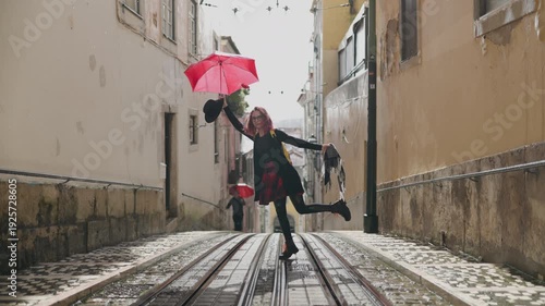 Happy young woman dancing under the rain on tram tracks