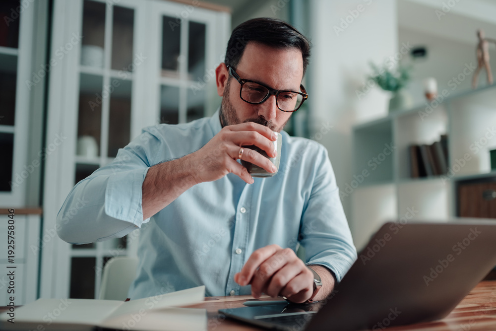 Fototapeta premium Professional man working remotely from home on laptop, drinking coffee and planning strategy