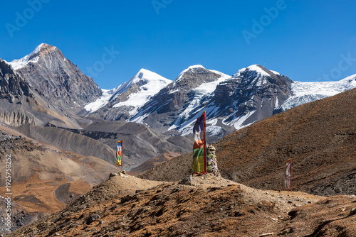 Colorful prayer flags stand on a barren ridge with dramatic snowcapped Himalayan peaks beyond, capturing spiritual culture of Nepal’s Annapurna region.