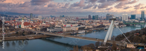 Panel kuchenny z motywem Aerial view of Bratislava, Slovakia, with SNP Bridge and UFO tower over the Danube. St. Martin's Cathedral rises at left, towers line the right bank, pastel dusk light.