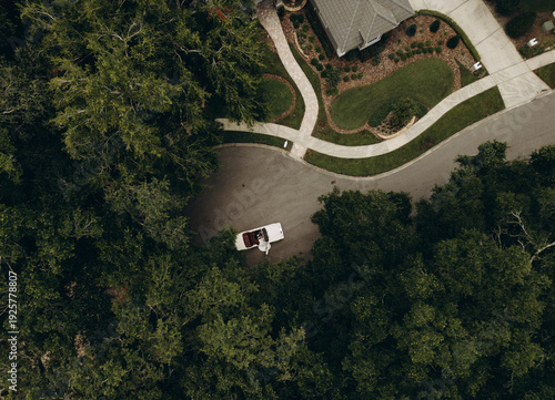 Top down drone shot of a modern suburban home with landscaped green yard and car parked on a quiet residential street surrounded by trees. Concept of real estate investment, 