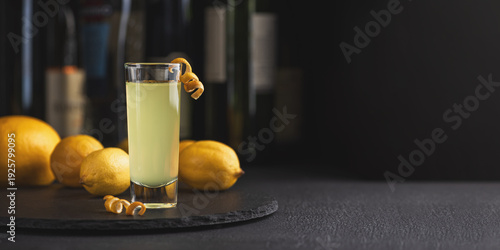 Foto Tall shot glass of limoncello garnished with a curled lemon peel, surrounded by