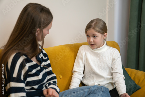 Two sisters sitting on a bright yellow sofa, engaging in a serious and supportive discussion about important family matters, fostering connection and understanding