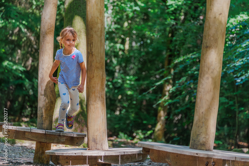 Cute running girl playing on wooden balance beams in forest park