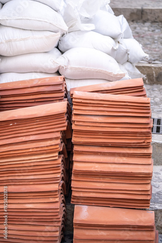 Stacked Terracotta Roof Tiles and White Sandbags at Construction Site Ready for Installation