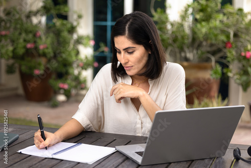 фотографія Focused adult student woman writing in copybook at laptop, listening to lecture,