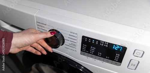 Fotografie Woman hand choosing program on automatic washing machine for laundry at home