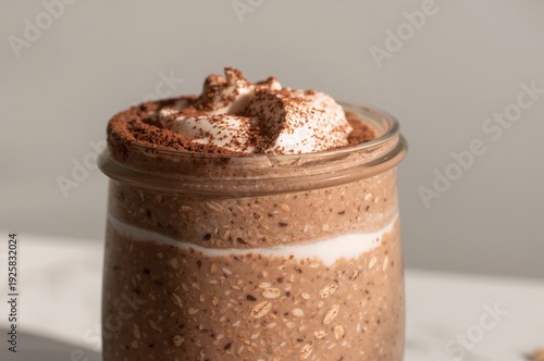 Layered cocoa oats with creamy topping in glass jar under soft natural light