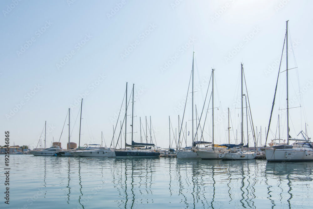 Fototapeta premium Row of white sailboats in sea port with water reflections