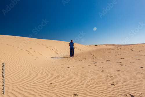 Принти на полотні Woman walking across the sand dunes of Corralejo Natural Park in Fuerteventura, Canary Islands, Spain